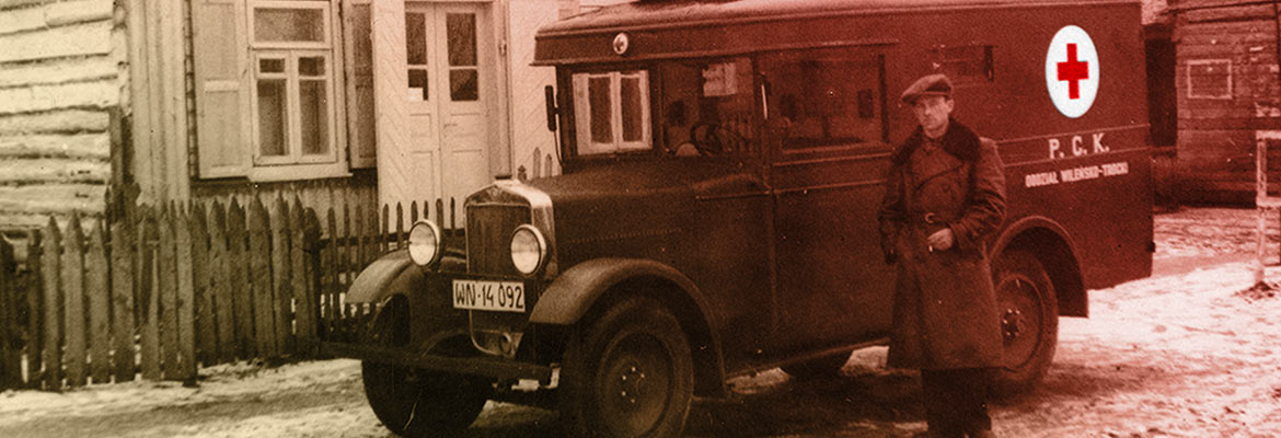 ambulans PCK, lata 30. XX wieku. przed ambulansem stoi mężczyzna w kaszkiecie