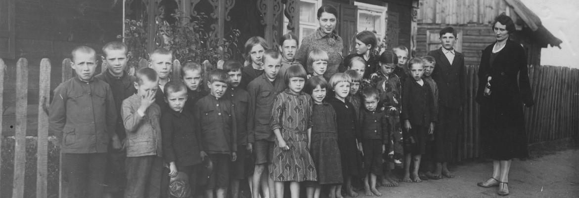 Grupa dzieci w wieku około 8-12 lat stoi przed drewnianym budynkiem wiejskiej szkoły. Żadne z dzieci nie ma butów. lata 30.