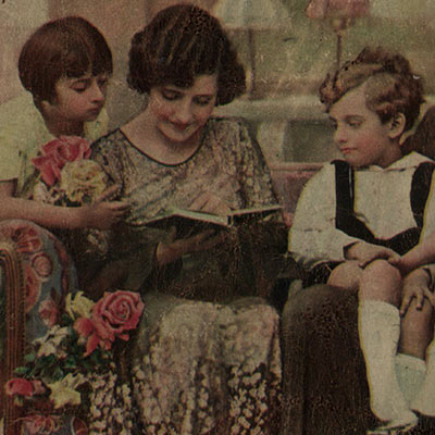dwoje dzieci z kwiatami przygląda się, jak ich mama ogląda książeczkę bądź notatnik - zapewne prezent od nich