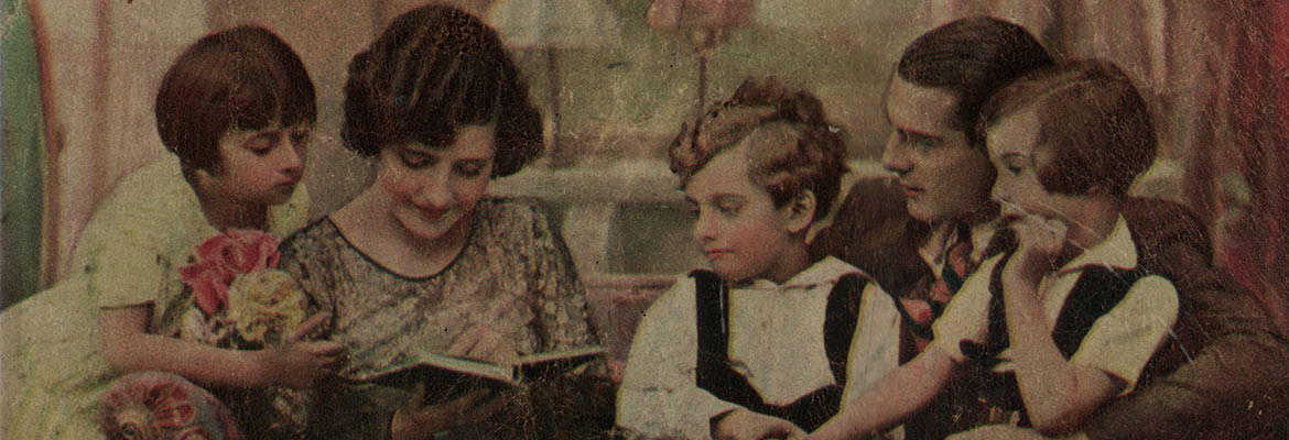 troje dzieci (dwoje siedzi na kolanach ojca) z kwiatami przygląda się, jak ich mama ogląda książeczkę bądź notatnik - zapewne prezent od nich